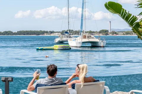 Pareja tomando algo frente a un catamarán en la bahía de Alcudia